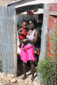 Woman stands with son outside makeshift home in Canaan, Haiti